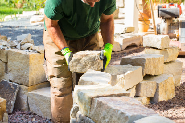 Mann baut Trockenmauer aus Sandstein