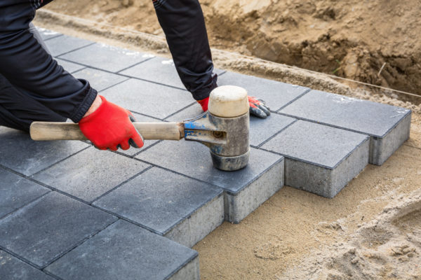 Hands of worker installing concrete paver blocks with rubber ham